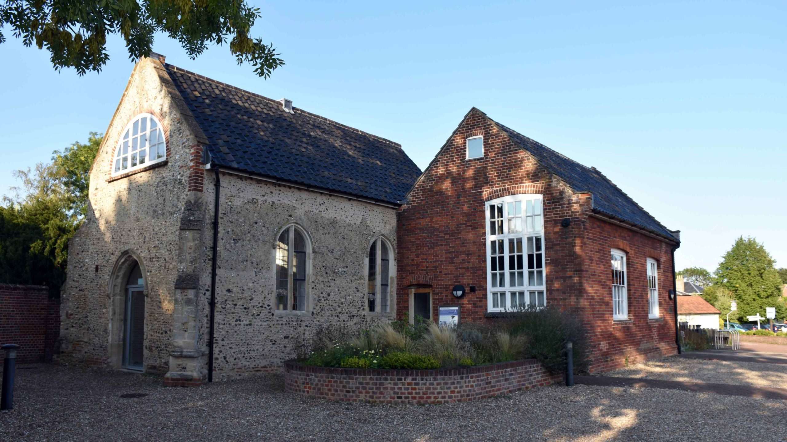 Exterior view of The Pennoyer Centre in Pulham St Mary, showing the restored historic brick and flint buildings under a clear blue sky.