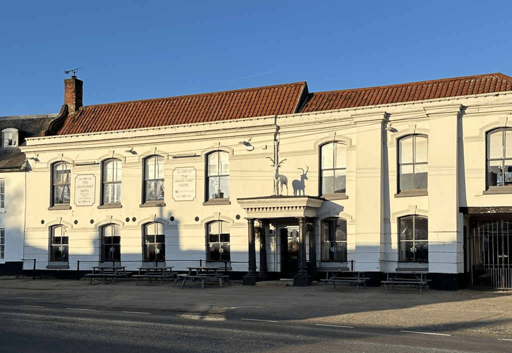The White Hart public house exterior, featuring a large historic cream-coloured building with a traditional façade, sash windows and a prominent entrance on a village high street.