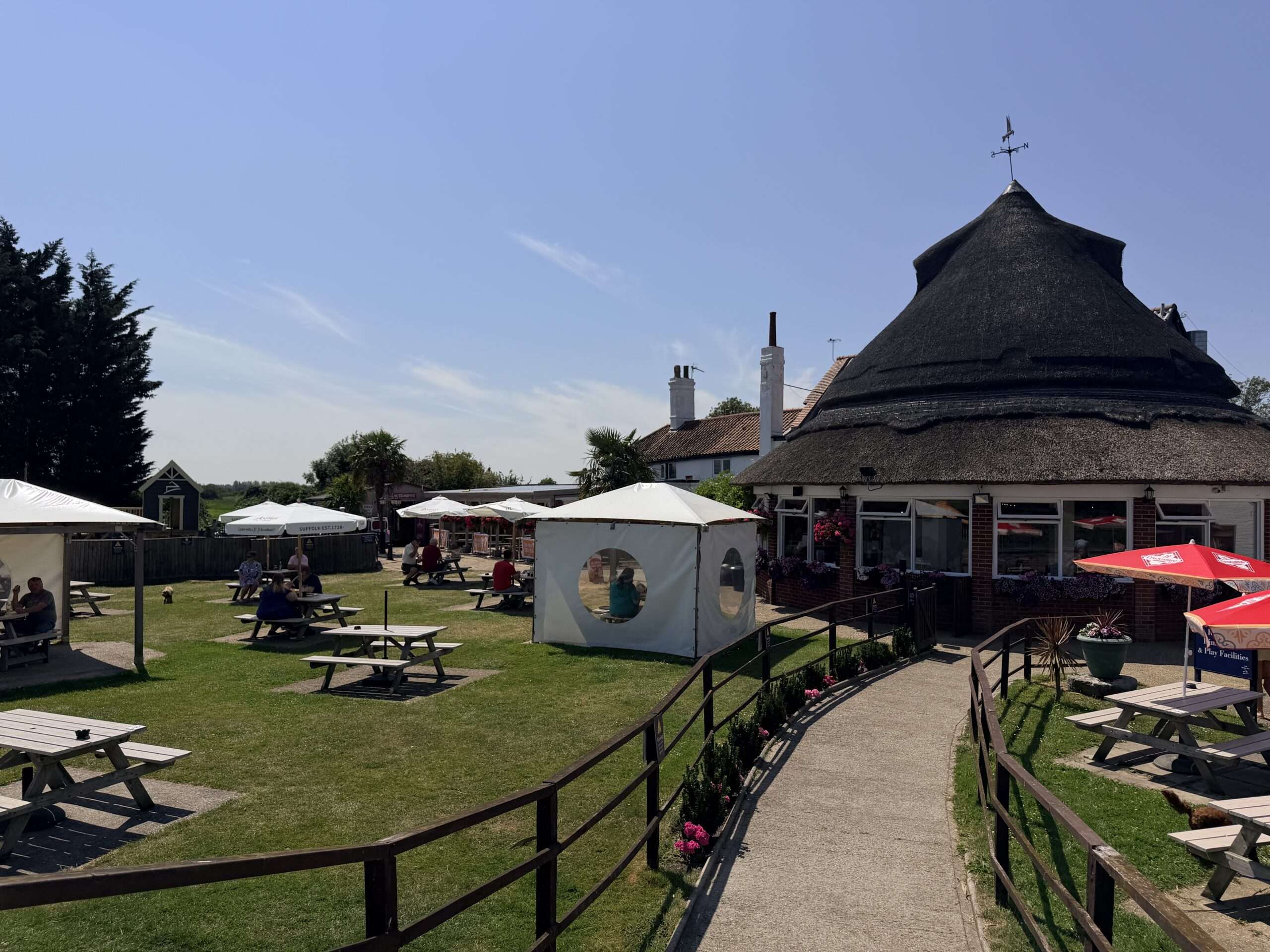 Outdoor seating and garden area at The Acle BridgeInn, with picnic benches, café facilities and views across the surrounding riverside landscape.