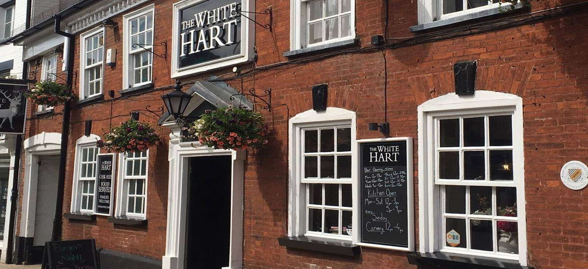 Exterior entrance of The White Hart, a traditional red-brick pub with hanging baskets and historic character.
