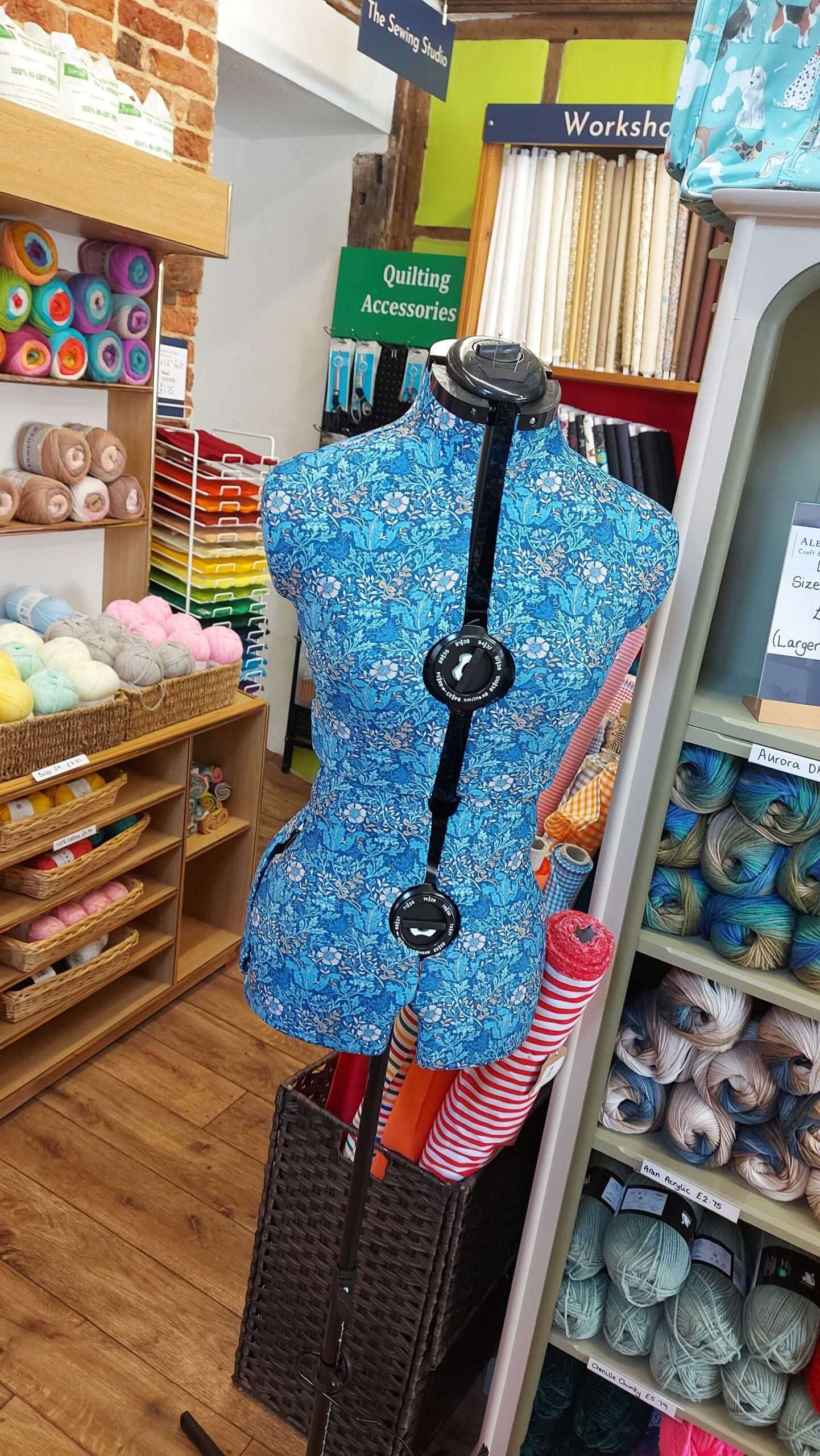 Dressmaker’s mannequin covered in patterned fabric displayed amongst quilting cottons and sewing supplies.
