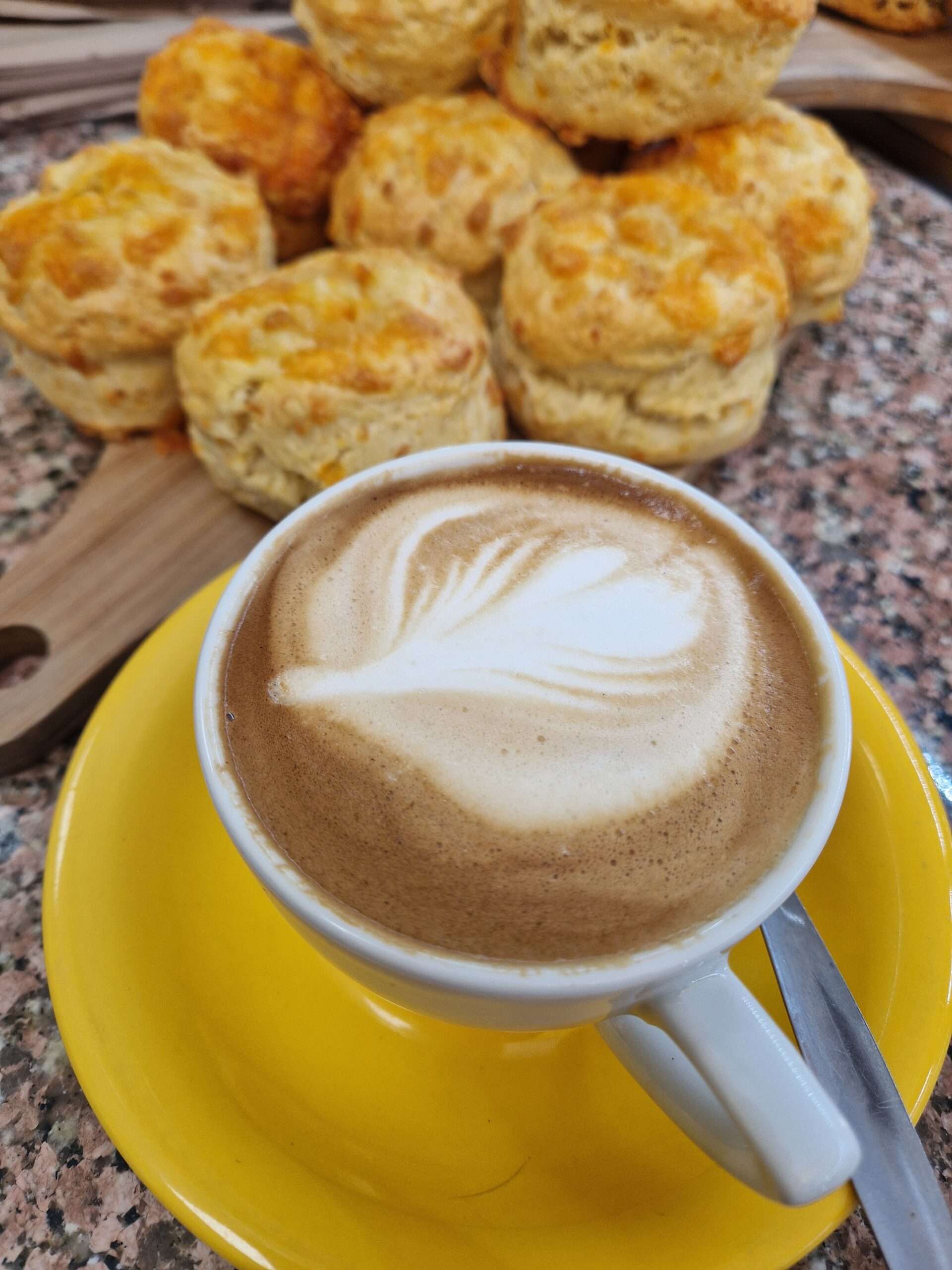Cup of freshly made coffee with latte art served alongside a selection of homemade cheese scones.