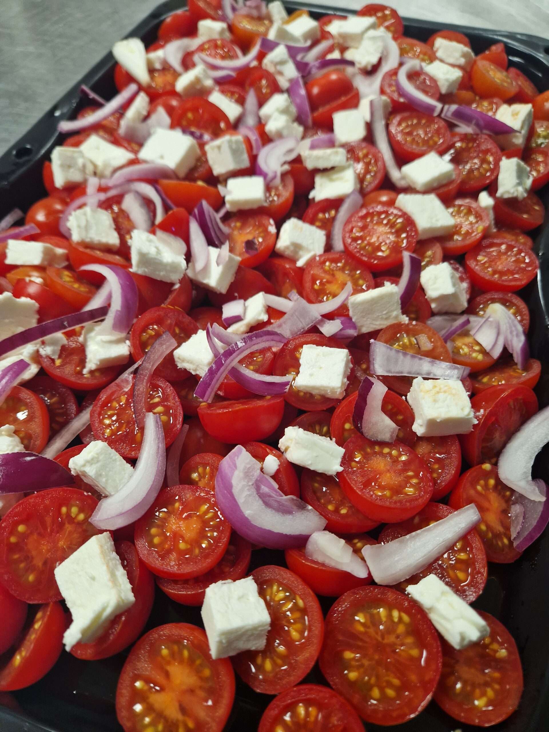 Fresh salad of cherry tomatoes, red onion and cubes of feta cheese served in a large bowl.