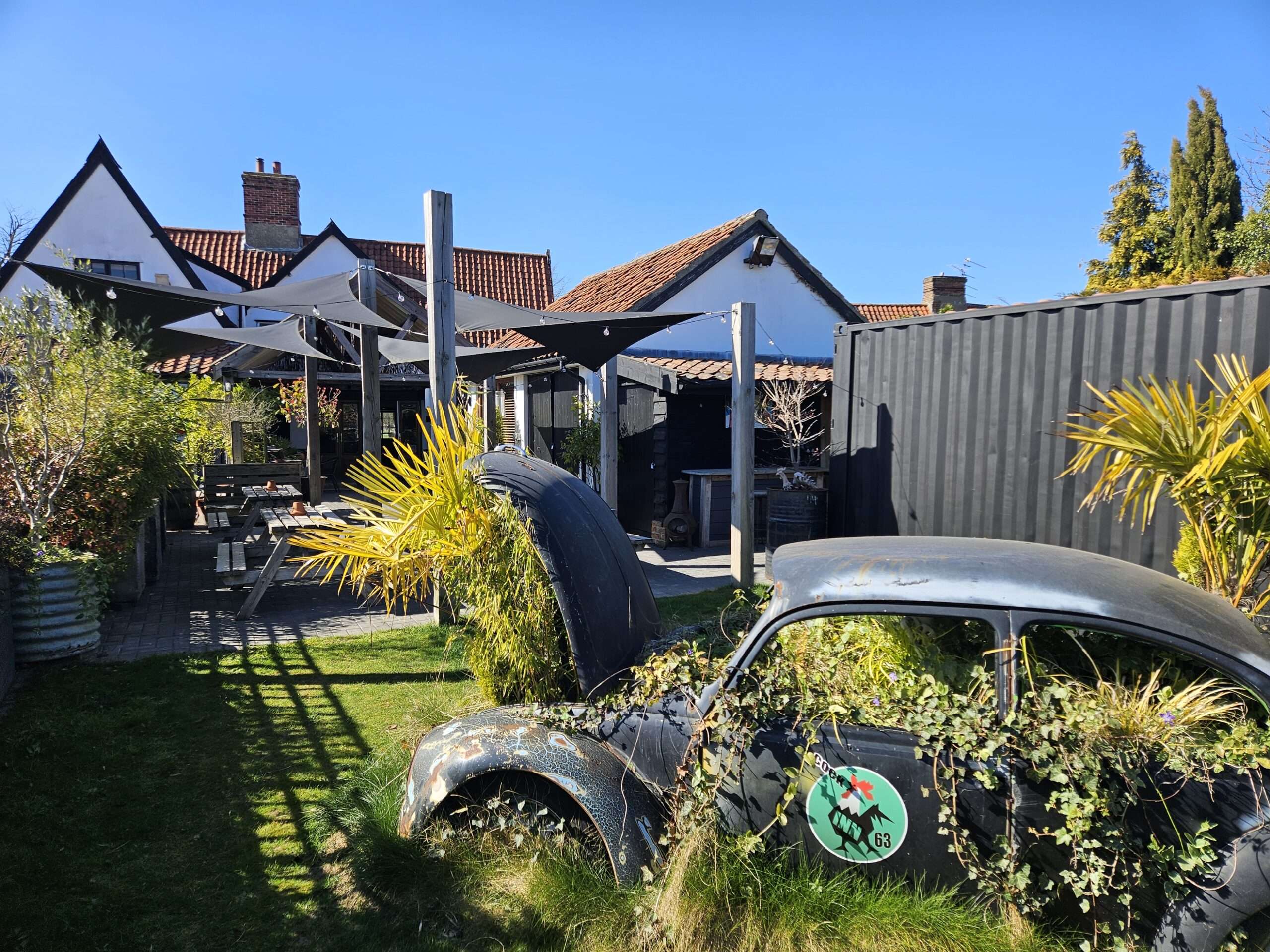 Landscaped outdoor terrace and seating area at the Cock Inn Diss overlooking the grounds on a bright day.