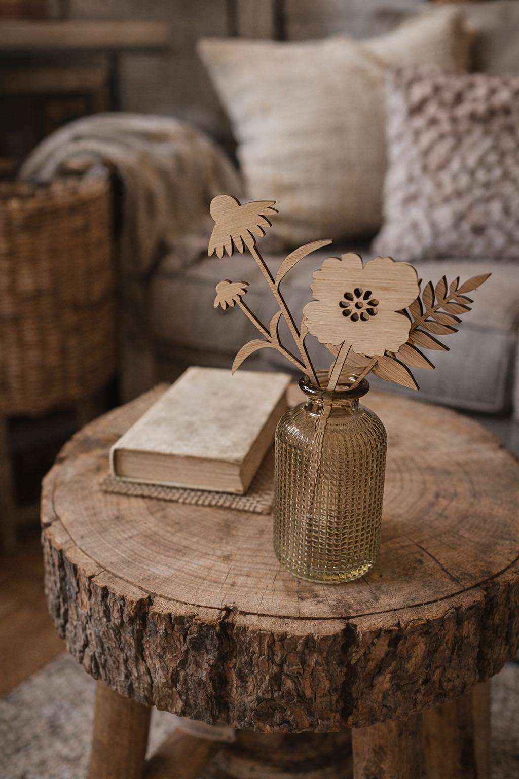 Decorative vase with wooden flower stems displayed on a rustic wooden surface alongside home accessories and soft furnishings.
