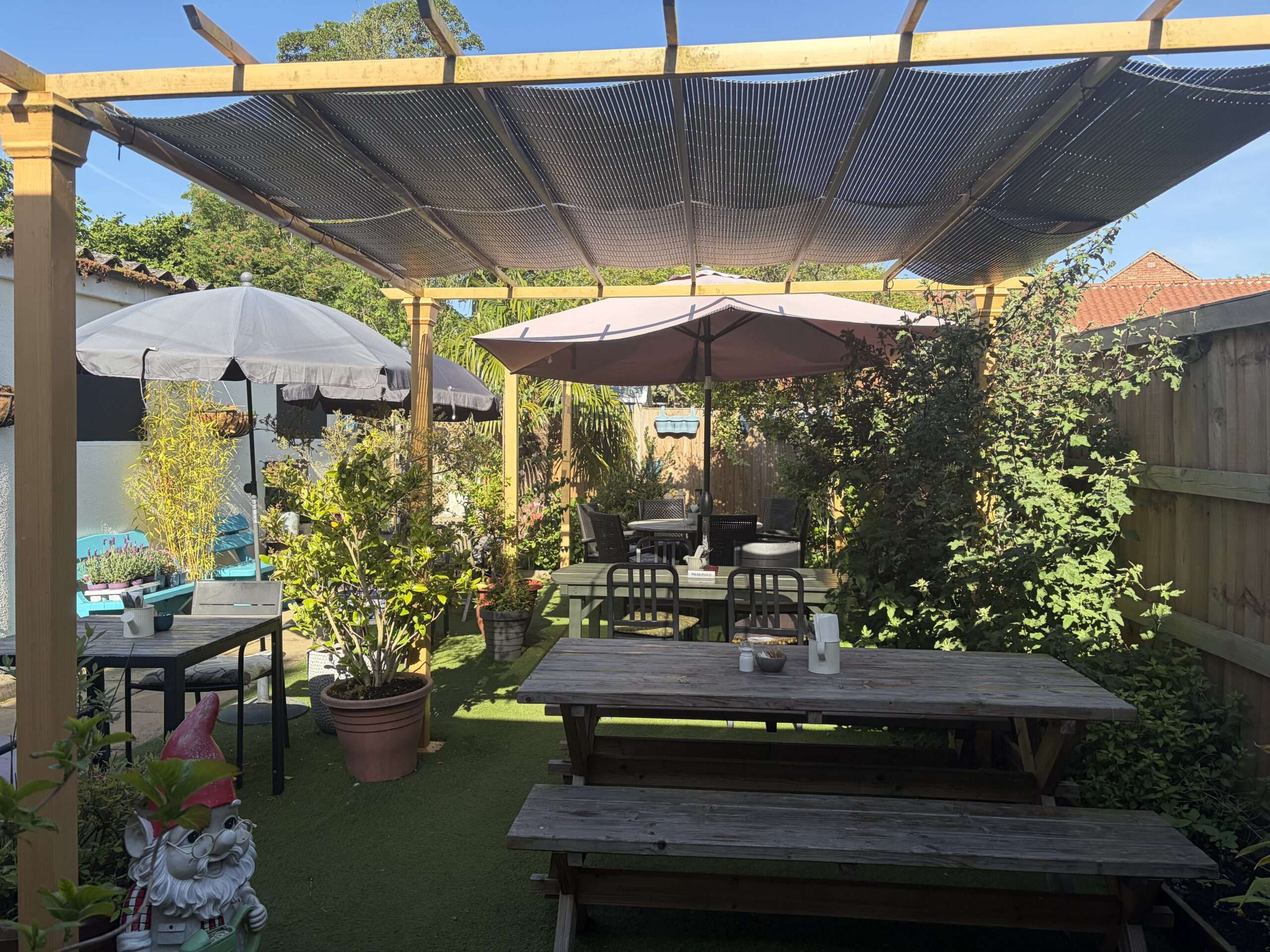 Outdoor café terrace with shaded seating, flowers and mature trees at Town Green Garden cafe