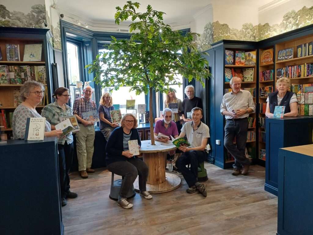 Visitors gathered inside Kett’s Books in Wymondham, surrounded by bookshelves and a decorative indoor tree.