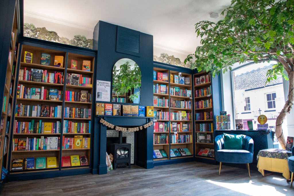 right bookshop interior at Kett’s Books, featuring floor-to-ceiling bookshelves, fireplace, mirror and indoor tree.