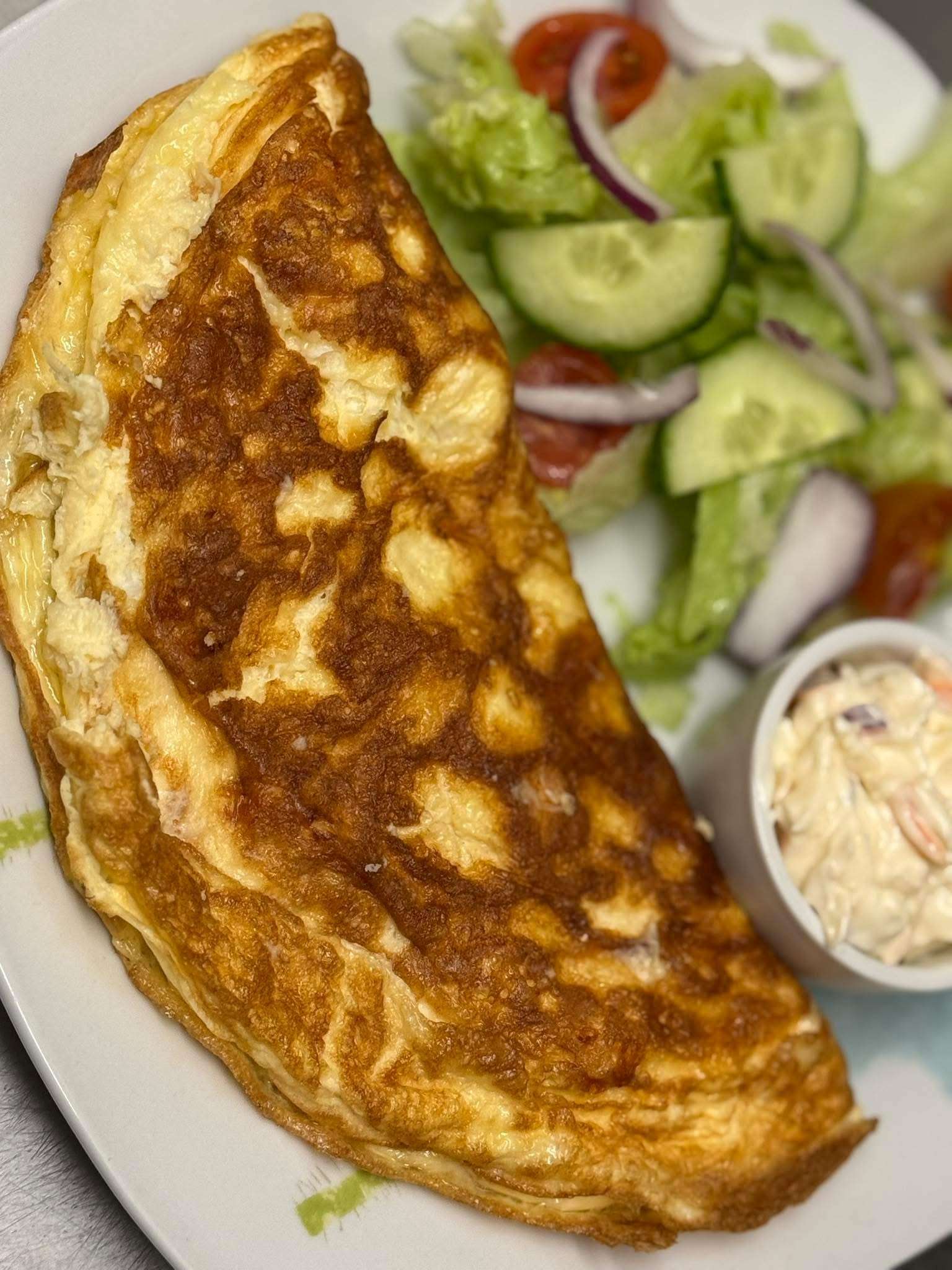 Close-up of an omelette served with fresh salad and sliced cucumber.