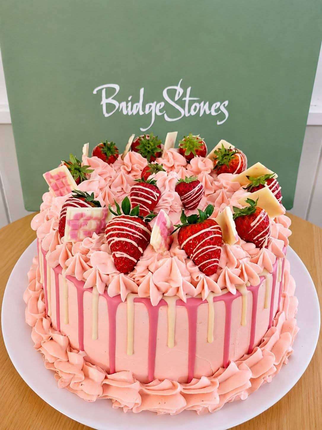 Pink celebration cake topped with fresh strawberries and Bridgestones branding.